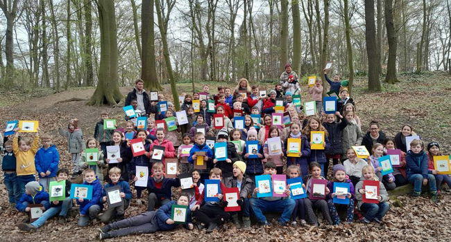 Zwischen Baumstämmen ist ein Seil gespannt, daran sind viele gemalte Bilder mit Klammern befestigt.